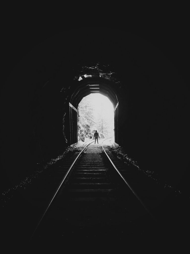 Man standing at the end of a tunnel, looking out at the bright light outside the dark tunnel